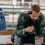 Unhoused person sitting on a bench and eating from an open can